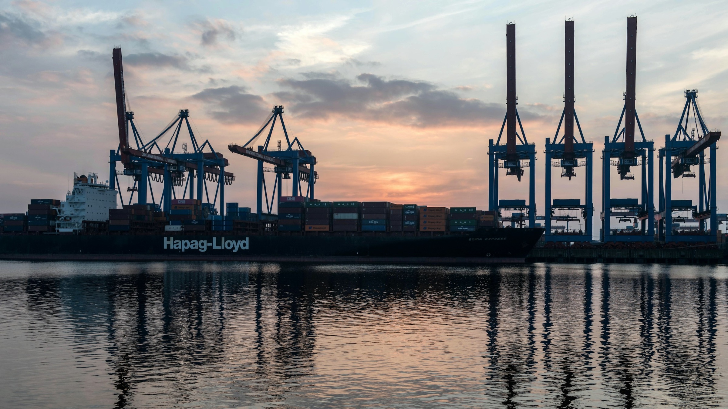 Container ship and port cranes at sunset in Hamburg, Germany